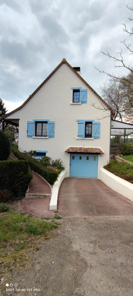 Maison de campagne blanche avec volets et porte de garage bleu pastel.