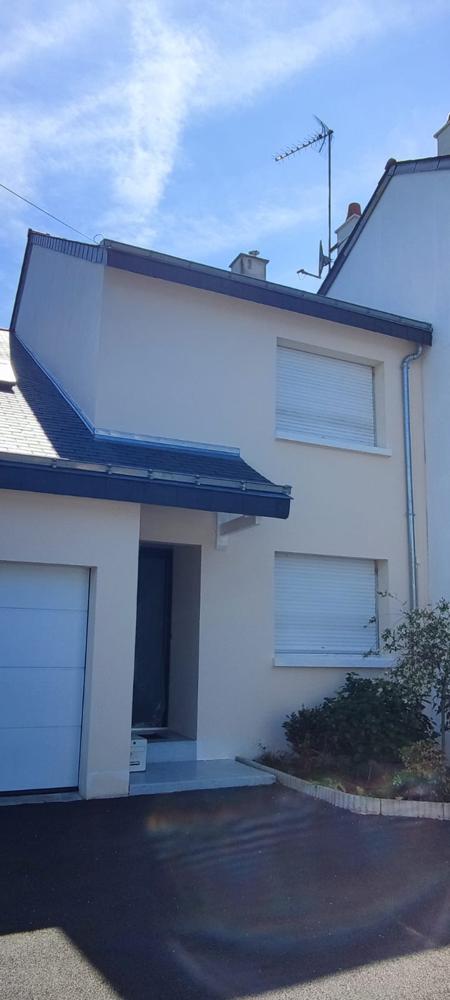 Façade moderne de couleur crème avec des volets roulants blancs et un toit en ardoise.