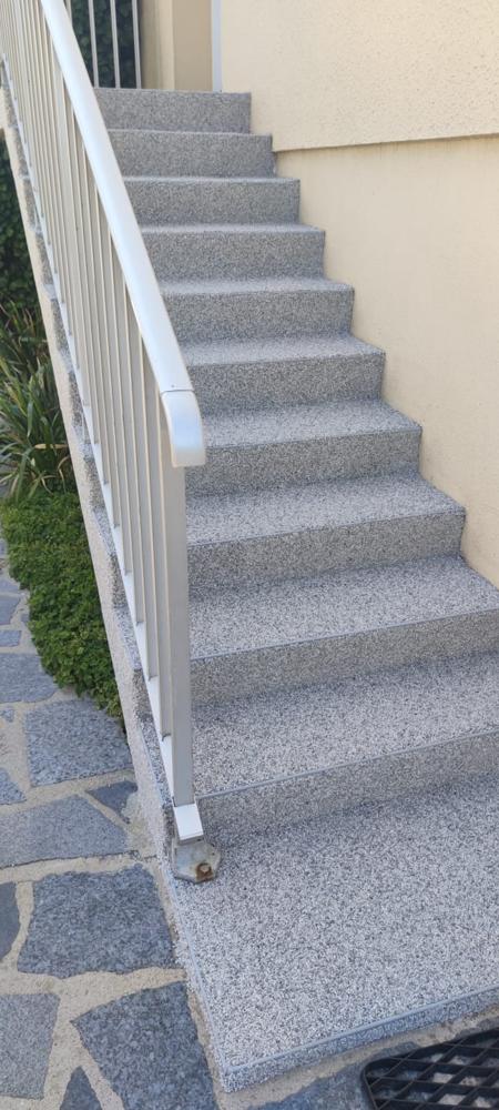 Long escalier extérieur recouvert d'un revêtement en résine et granulat de marbre gris.