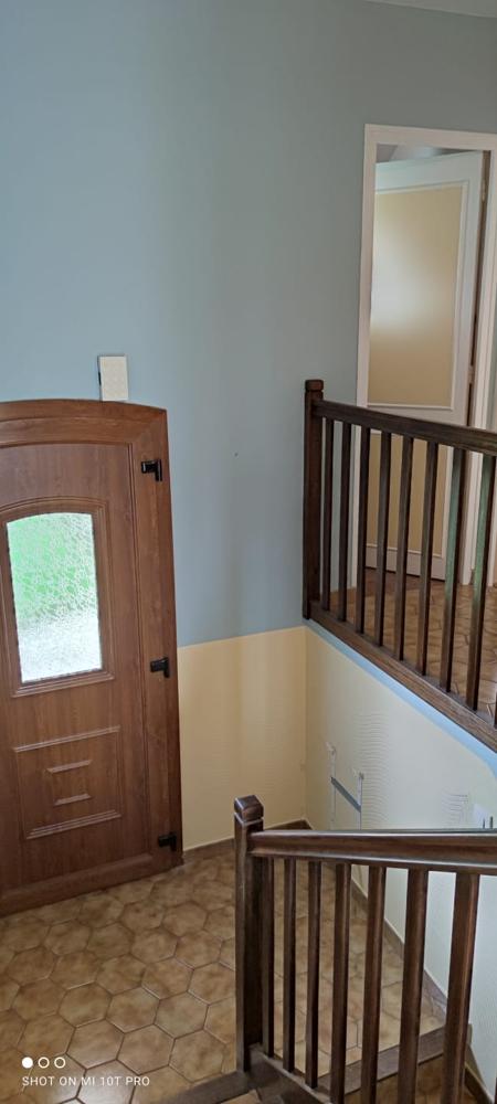 Un escalier avec une rampe en bois foncé et un mur bicolore bleu clair et jaune. Une porte en bois marron avec un panneau en verre est sur la gauche.