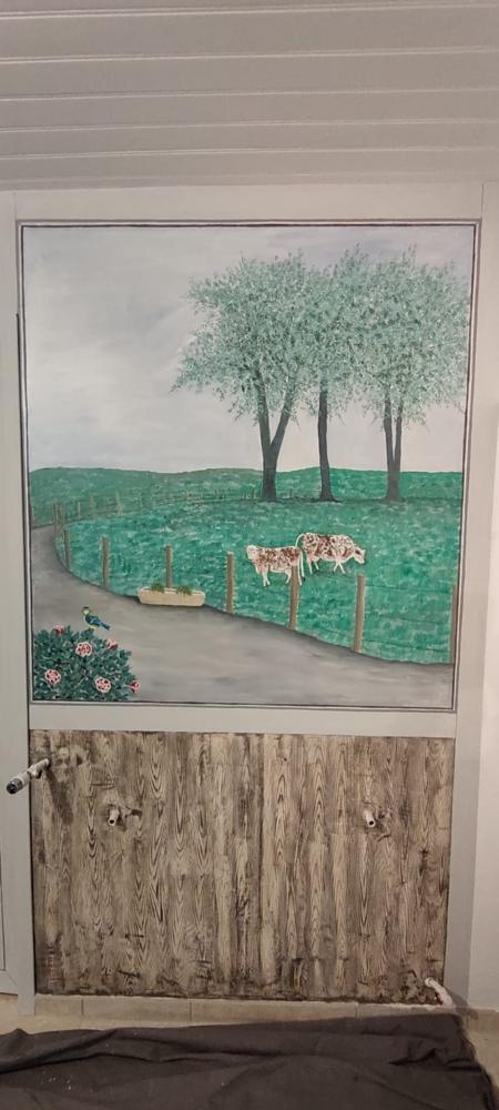 Une grande peinture murale d'une scène de champ avec deux vaches, des arbres verts et une route, peinte sur la moitié supérieure d'une porte ou d'une armoire. La moitié inférieure est peinte pour ressembler à une surface en bois rustique.
