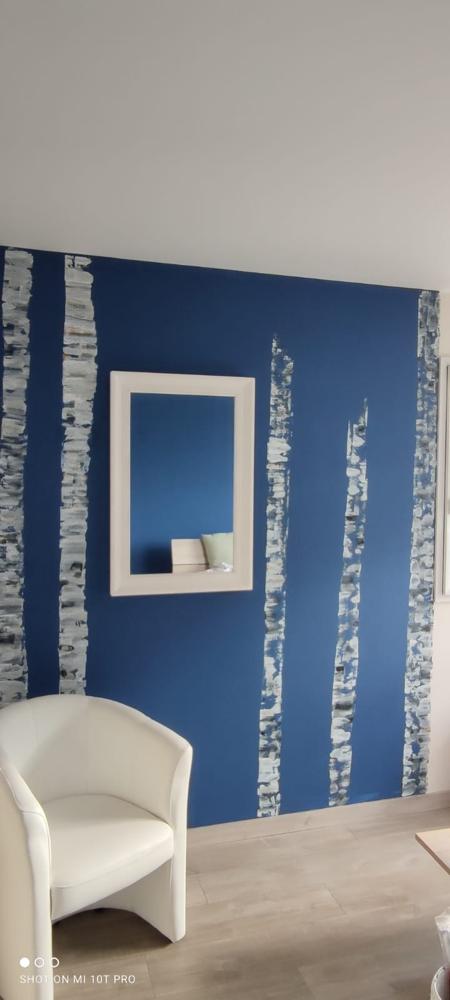 Une pièce fraîchement peinte avec un sol aspect bois clair posé en diagonale, une petite section de carreaux décoratifs au bas et des murs blancs et lumineux avec de grandes portes vitrées à l'extrémité.