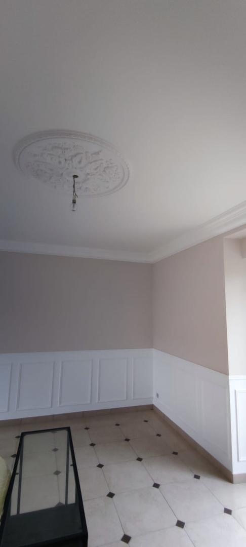 Salon élégant avec murs beige rosé, lambris blancs, rosace décorative au plafond et carrelage à motifs