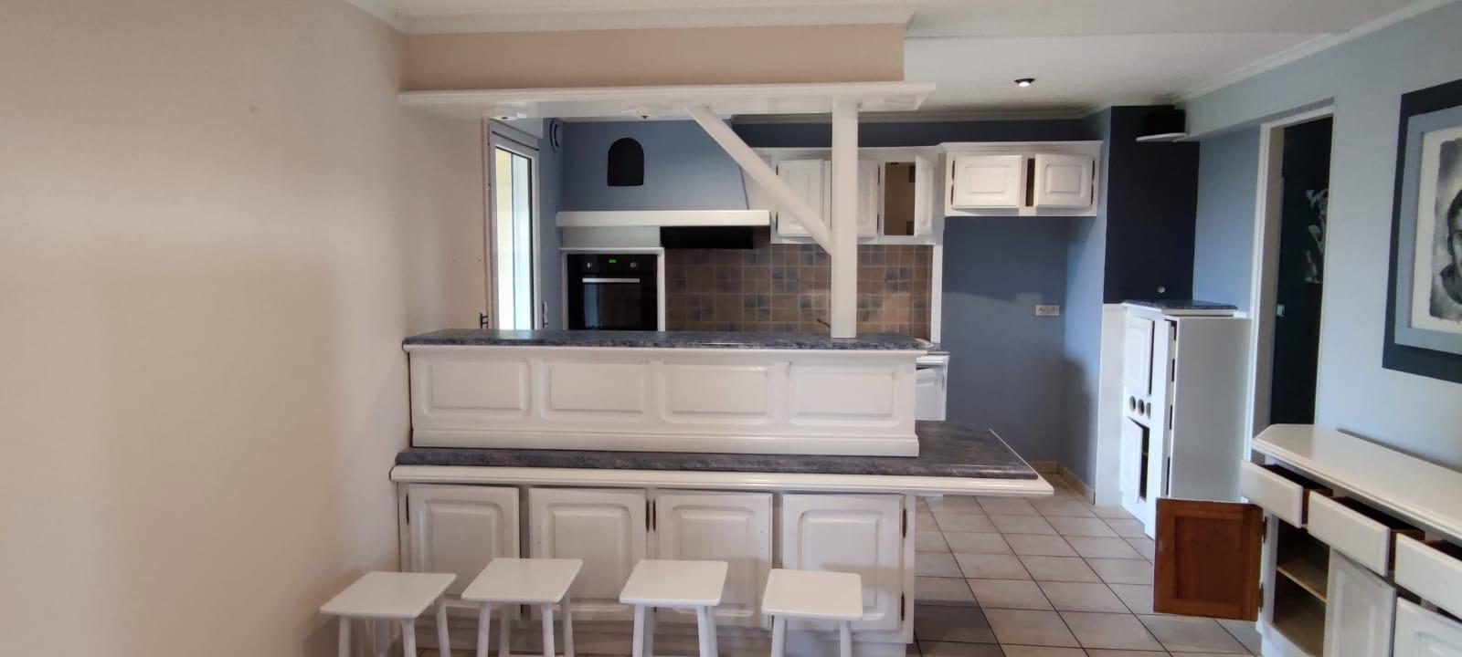 Une vue d'un coin cuisine avec des armoires blanches et un comptoir gris et blanc. Les murs de la cuisine sont peints d'un bleu profond et la pièce au premier plan est d'un beige clair.