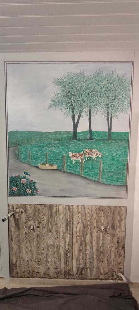 Une grande peinture murale d'une scène de champ avec deux vaches, des arbres verts et une route, peinte sur la moitié supérieure d'une porte ou d'une armoire. La moitié inférieure est peinte pour ressembler à une surface en bois rustique.