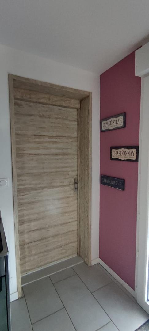 Une porte intérieure avec un encadrement et un battant à l'aspect bois clair texturé, jouxtant un mur rose orné de plaques décoratives sur le thème du vin.