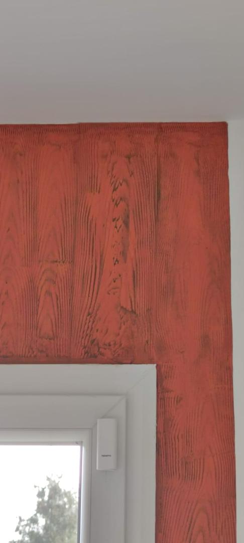 Gros plan sur une peinture décorative à effet faux bois rouge avec des veines sombres détaillées autour d'un encadrement de fenêtre blanc.