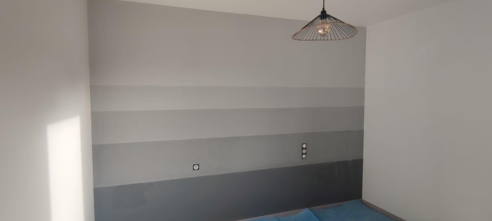 Un mur décoré d'un dégradé de bandes horizontales allant du gris très clair au gris anthracite foncé sous un luminaire design.
