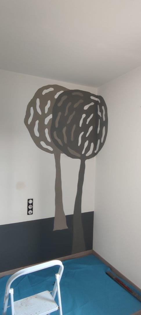 Peinture murale décorative représentant deux arbres stylisés dans des tons de gris et beige sur un mur blanc avec un soubassement sombre.