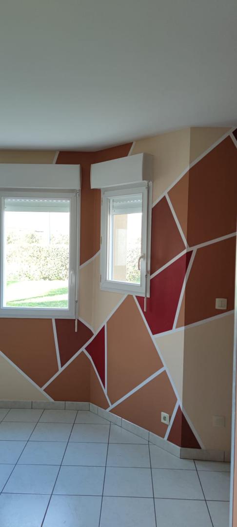 Salon avec mur décoratif géométrique multicolore orange, rouge et beige sur carrelage gris