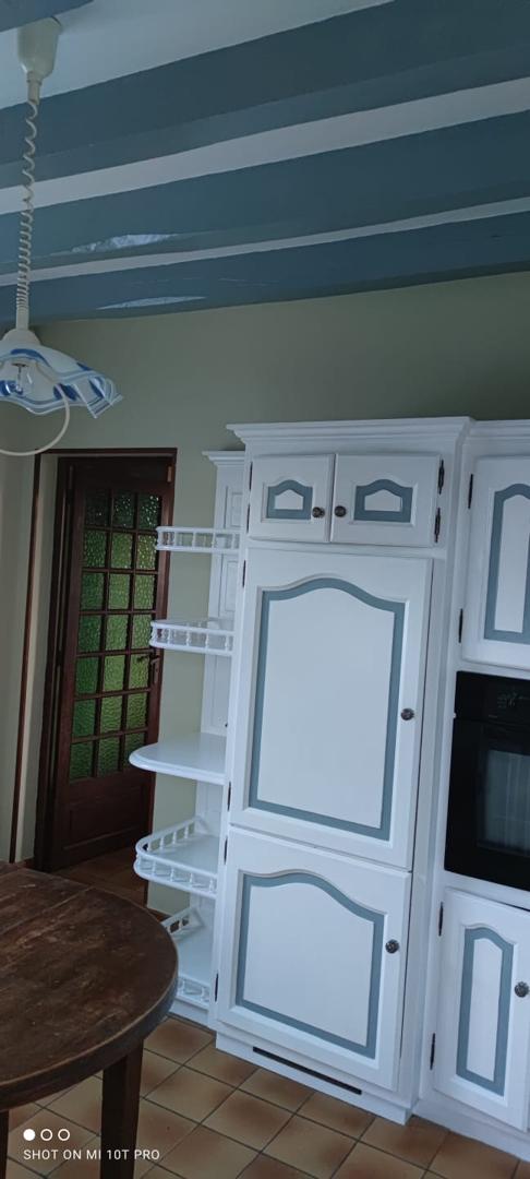 Cuisine campagnarde avec poutres peintes en vert, meubles blancs traditionnels et carrelage au sol