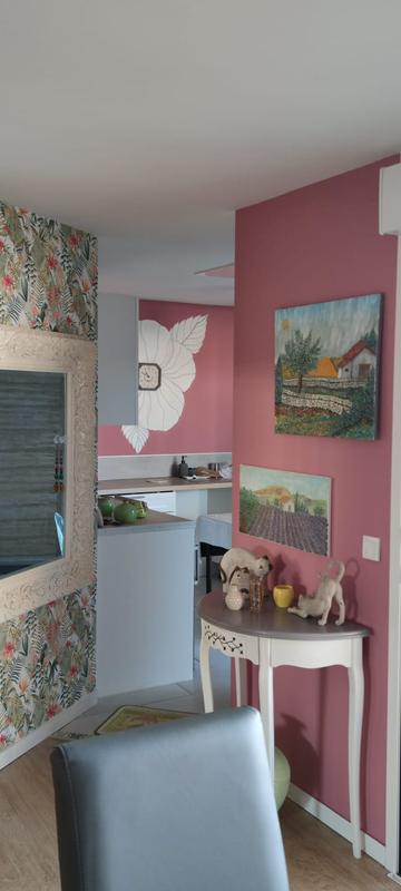 Vue d'un intérieur décoré avec un mur d'accent rose framboise, du papier peint tropical à gauche et une console blanche de style classique sous des tableaux de paysages.