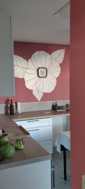 Mur de cuisine rose avec une grande fleur blanche peinte à la main entourant une horloge centrale au-dessus du plan de travail.